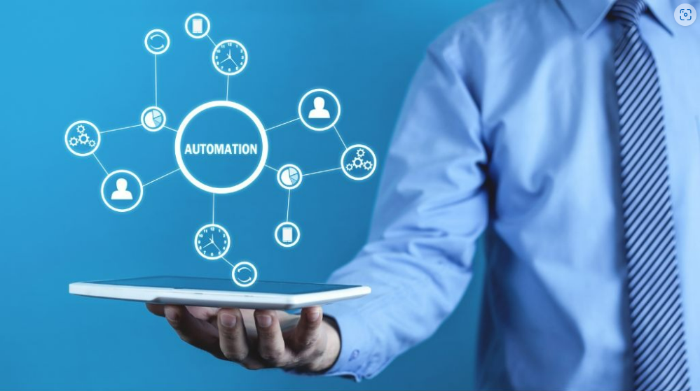 A person in a blue shirt holds a tablet with a glowing "AUTOMATION" diagram floating above it.